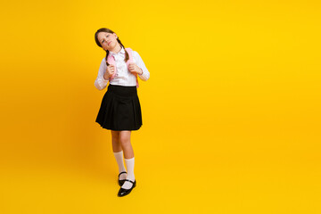Cheerful schoolgirl in a traditional uniform on a vibrant yellow background ready for a day of...