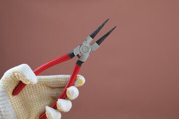 Hand wearing gloves holding snap ring pliers with red rubber handle grip on isolated background.
