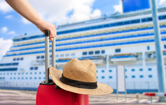 For travel and vacations purposes, a simple modern suitcase in red color at ship in a port with a straw hat.
