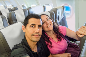Happy tourist taking selfie inside airplane.Cheerful couple on summer vacation .Passengers boarding...