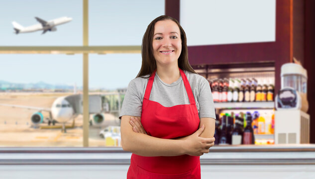 Hispanic female barista with red apron standing in the coffee shop at an airport - Powered by Adobe