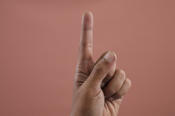 Faceless man doing the peace sign with her fingers against brown wall, Hand of Caucasian young man showing fingers over isolated brown background counting number 1 showing one fingers.