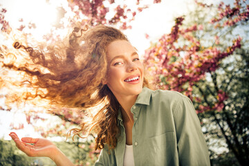Beautiful young woman smiling joyfully outdoors in a blossoming park under the daylight with...