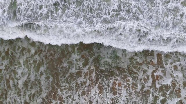 Aerial bird's eye view of foaming ocean waves from above at Praia da Am&aacute;lia, Costa Vicentina, Portugal. Captured in slow motion, revealing the textures and movement of the sea.