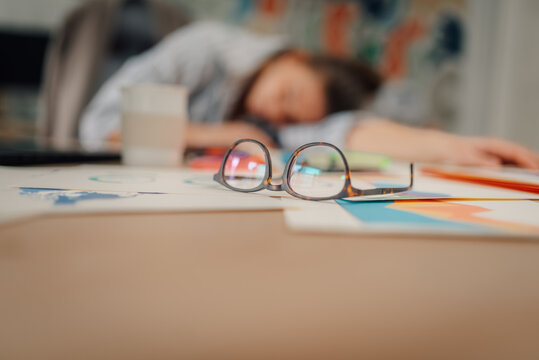 Businesswoman sleeping at workplace after working late night on financial reports - Powered by Adobe