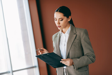 Professional businesswoman reviewing documents in modern office with confident demeanor and stylish...