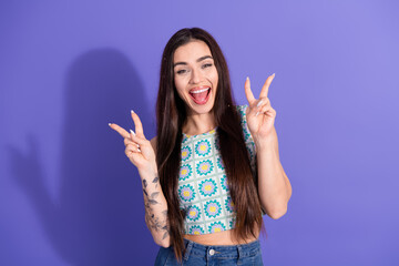 Cheerful young woman with long hair showing peace gestures on contrasting vibrant purple background
