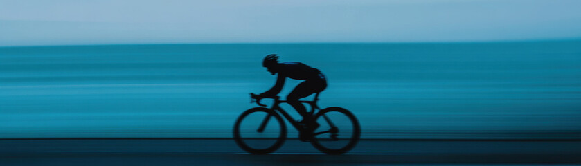 Fototapeta premium Cyclist in aerodynamic skinsuit glides effortlessly along coastal road, surrounded by serene blue backdrop. motion captures essence of speed and tranquility