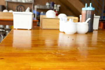 A wooden dining table with condiments, including white shakers and a blue squeeze bottle, in a blurred restaurant setting.