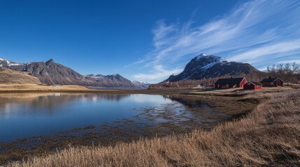 Amazing view in Norway! Red cabins sit by a fjord, with huge mountains all around under a bright blue sky. This is Lofoten, Norway.
