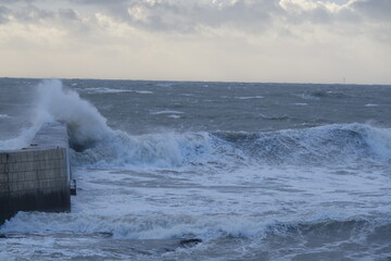 A strong wave is hitting the jetty on a stormy day. Batz-sur-Mer, France - November 2, 2023. 