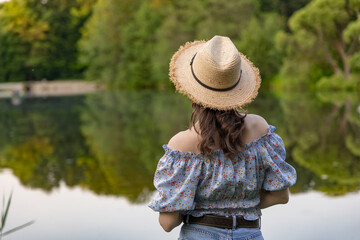 A woman in a cowboy hat, a blouse with a floral print and jeans stands against the background of a pond with water lilies. © night87