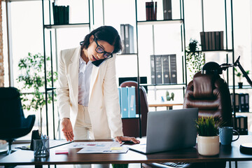Confident businesswoman in a modern office environment multitasking with technology and documents...