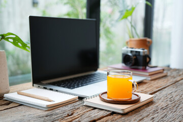 Orange juice and a laptop and notebook, cozy workspace by the window
