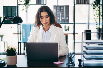 Businesswoman in formal attire working on a laptop at her office, focusing on professional tasks in...