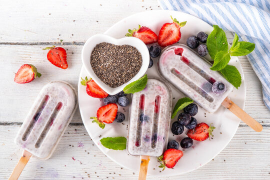 Chia seeds ice cream lolly popsicles, homemade healthy detox gelato with creamy yogurt, chia seeds and fresh summer fruit and berries, on white table copy space