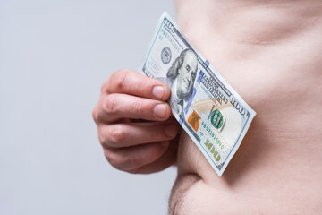 Close-up of a male hand with hundred dollar bill on a bare belly. Conceptual image for themes of...