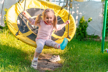 Little child swings on a round swing in summer