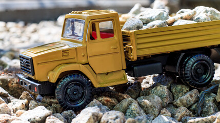 A vibrant yellow toy dump truck, brimming with small, realistic stones, navigates a miniature...