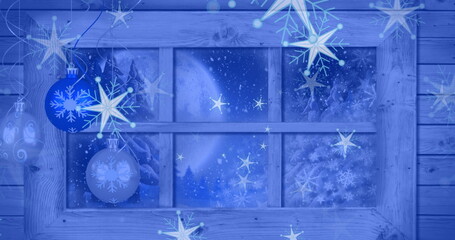Displaying window with frost in cabin, hanging blue snowflake baubles before moonlit pine forest