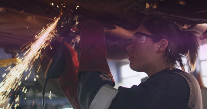 Mechanic grinding chassis with angle grinder in workshop, sparks flying, wearing gloves, copy space