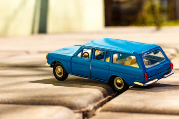 A vibrant blue vintage station wagon toy car, with its classic lines, parked on a textured paved...