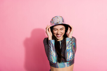Stylish young woman in a trendy metallic outfit posing with a dazzling disco hat against a vibrant pink backdrop