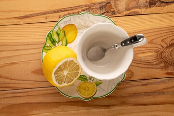 Ceramic cup on a ceramic saucer with lemon on a wooden table, top view.