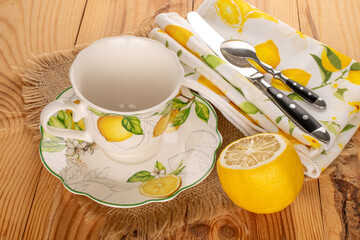 Ceramic cup on a ceramic saucer with lemon on a wooden table, top view.
