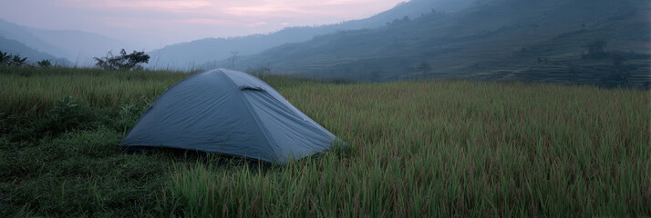 Tent set up in serene rice field at dusk, surrounded by misty mountains