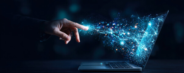 A hand reaches toward a laptop, creating a stunning display of light and data particles, symbolizing the connection between technology and creativity in the digital age.