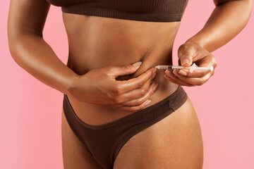 Closeup of young African American woman injecting herself in belly with syringe in underwear on...
