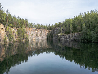 Serene landscape photograph of Syrjän Lagoon in Finland, showing calm water reflecting the steep quarry cliffs and surrounding forest. 