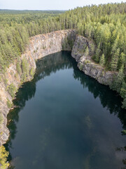 High-resolution aerial image of Syrjän Lagoon, a former quarry filled with deep blue water, surrounded by vertical rock walls and lush pine forest in Finland.