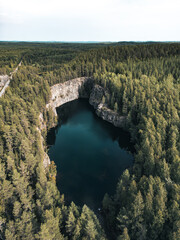 Aerial photo of Syrjän Lagoon, a secluded forest lake surrounded by steep rocky cliffs and dense pine woodland in Finland. The turquoise water contrasts beautifully with the green forest.