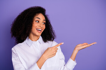 Attractive young woman in a white shirt gesturing and pointing on a purple background in a stylish...