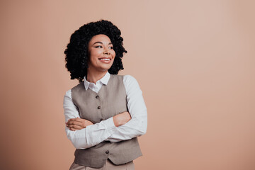 Confident young professional woman in formal attire with crossed arms posing on beige background...