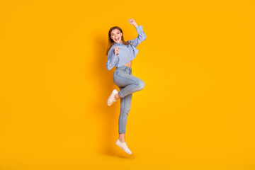 Fototapeta na wymiar Energetic young woman jumping with cheerful expression in casual outfit, showcasing fun and positivity against a yellow backdrop
