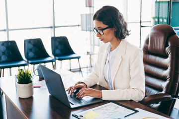 Professional businesswoman at work in a corporate office sitting at a desk using a laptop computer,...
