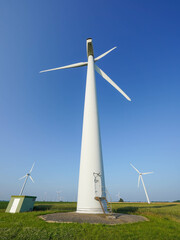A wind turbine stands tall in a green field under a clear blue sky
