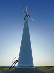 A large wind turbine rises against a clear sky with a stairway leading to its base