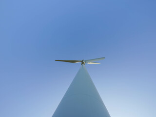A modern wind turbine captured from below against a clear blue sky