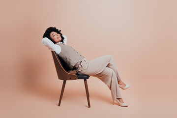 Elegant businesswoman relaxing in chair with stylish outfit and beige background, showcasing modern...