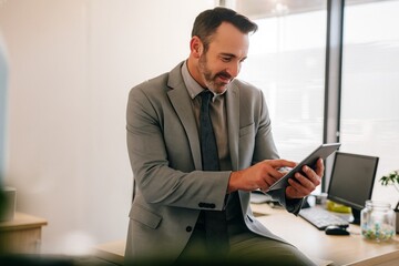 Fototapeta premium Successful Businessman Using Tablet Modern Office Professional Gray Suit Technology Digital Device Entrepreneur Working Man Serious Concentrated Happy Smiling Workplace Desk Indoors data online future