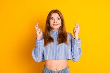 Young woman with crossed fingers on a yellow background expressing hope and positivity, showcasing...
