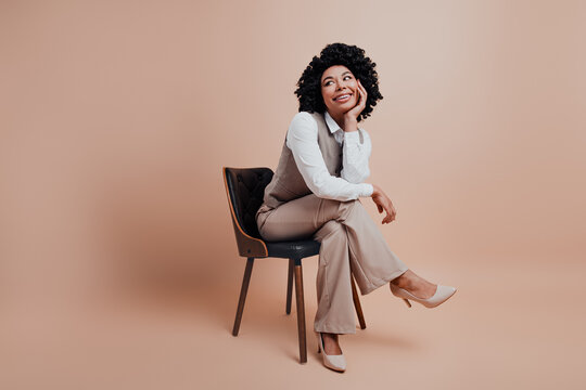 Fototapeta Young professional woman sitting confidently on chair against neutral background expressing charm and elegance