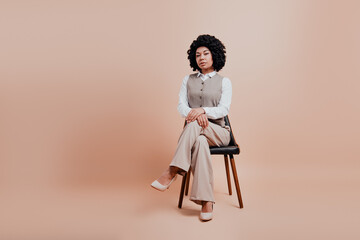 Confident young businesswoman sitting on a stylish chair in formal beige attire with a professional...