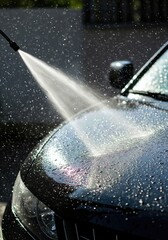 Close-up of washing a car with a high-pressure water sprayer, cleaning the vehicle's hood at a car wash