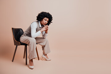 Confident businesswoman sitting on a chair with a pensive gesture wearing formal attire against a...