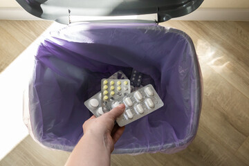 Female hand discarding blister packs into trash bin. Concept of disposing expired medication,...